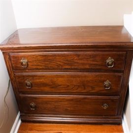 Ethan Allen Oak Small Chest: A small Ethan Allen oak chest of drawers. The three-drawer unit has Colonial styling and uses two antiqued brass-toned round pulls on each drawer. It is stained a dark brown. This item matches 17COL157-037.