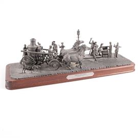 Ronald Hinote Metal Sculpture "Fire on Main Street": A metal sculpture titled Fire on Main Street by artist, Ronald Hinote. This sculpture depicts a chaotic, early 20th century street scene. Depicted is a crowd of people gawking at a fire engine, pulled by horses. This piece is signed in-mold to the verso and presented atop a wooden base. Affixed to the base is a silver tone plaque that specifies the title and artist of this work.