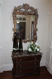 Bernhardt marble-topped chest, Currey & Co. decor obelisks, ornate mirror with distressed gilt finish, faux flower arrangement 