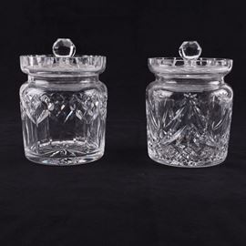 Waterford Crystal Jars: A pair of crystal jars by Waterford. They contain ball finials with cut glass lids. The bodies feature cut diamonds. One has stars and ray patterns. They have starburst designs to the bases. Pieces marked to undersides.