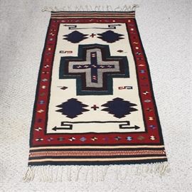 Handwoven Wool Rug: A handwoven wool rug. This runner features a neutral ground with a dark red and black border and dark green accents. It is geometric in pattern.