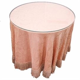 Pressed Wood Table with Full-Length Skirt: A pressed wood table with skirt. This piece has a circular top on a four panel base. The panels each have a concave curve to the outside and are set in an X. The full length salmon colored skirt has a leaf print all over, with fringe around the ends. It comes with a removable glass top.