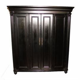 Black Wooden Computer Armoire: A black wooden computer armoire. It has crown molding to the top, above two doors, each with double panel design to the front with brass tone pulls, flanked by reeded columnar front stiles, all raised on bun feet. Inside, it has a large open section over shelving and drawers to the bottom.