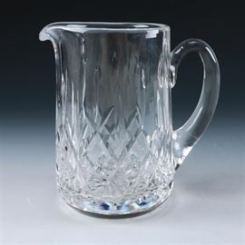 Waterford Lismore Water Pitcher: A Waterford crystal Lismore pitcher. This cut crystal pitcher from Waterford features a small pout spout, large thick curved handle and a diamond motif near the base. Pitcher has a starburst accented base and is marked on the bottom.
