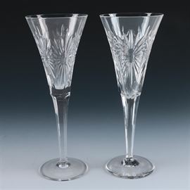 Pair of Waterford "Millennium Series" Fluted Crystal Champagne Glasses: A pair of Waterford Millennium Series champagne glasses. This pair features two fluted crystal glasses cut in the Health pattern. Each glass features tapered cups, fluted stems, and circular bases. The glasses are acid stamped “Waterford” to the underside.