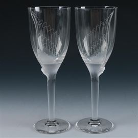 Lalique "Ange" Champagne Flutes: Lalique Ange champagne flutes. This pair of champagne flutes from Lalique crystal are presented in the Ange pattern with etched angel wings leading down to molded base relief angel heads that rise above the narrow stems and flaring bases. The glasses are marked to the underside “Lalique France.”