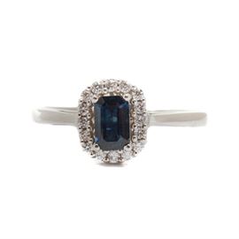 10K White Gold Sapphire and Diamond Ring: A 10K white gold sapphire and diamond ring. This ring features an emerald cut blue sapphire center stone with a halo of brilliant cut diamonds in a pierced gallery cathedral setting.