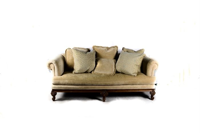 Contemporary Louis XV Style Sofa: A contemporary Louis XV style sofa. This upholstered piece features a straight crest rail with rolled arms, flanking a cushion seat over a wooden apron rising on decorative carved cabriole legs terminating on pad feet. The legs include acanthus leaf detail. The sofa is upholstered in a beige fabric. Also included are matching accent pillows. There are no visible maker’s marks.