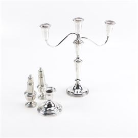 Weighted Sterling Silver and Pewter Tableware: A pair of weighted sterling candle holders and weighted pewter shakers. This grouping offers a pair of weighted sterling silver candle holders by Empire, one with a round base, turned column with a single candle cup, and a pair of arms each with a candle cup. The other holder is short, and features a round base with a single candle cup, both marked to the underside. There is also a pair of pewter shakers in a classic shape marked “Empire, Pewter, Weighted”.