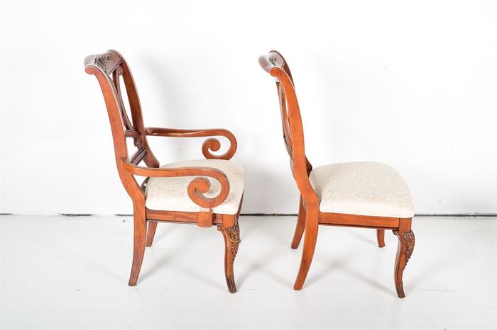 Eight Cherry and Upholstered Dining Chairs: A set of eight cherry dining chairs with upholstered seats. The chairs feature arched top rails with a carved accent, back rests with oval, bead trimmed openings set inside three scrolled braces. The set included two captain’s chairs with scrolled arms, The chairs stand on cabriole front legs and saber back legs. The chairs are upholstered in tone on tone cream colored, machine embroidered fabric with matching trim. Companion dining table under 17LEX185-095, sideboard 17LEX185-092, and two-piece hutch 17LEX185-096