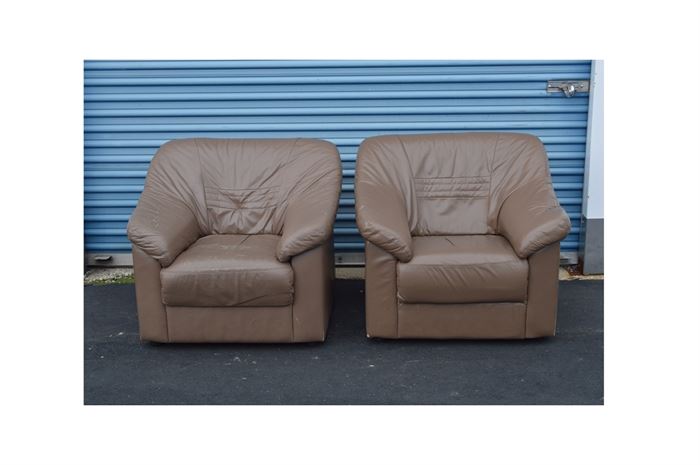 Pair of Bonded Leather Club Chairs: A pair of bonded leather club chairs. Each chair features a pillowed design with straight crest sloping to angled arms with panel sides and flat apron front. The chairs are upholstered in a tan tone bonded leather and include quilted accent on the seat back.