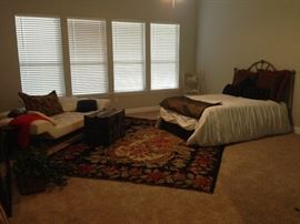 Queen-size bedframe with modern white leather sofa and large area rug. Trunk as coffee table. Staging furniture.