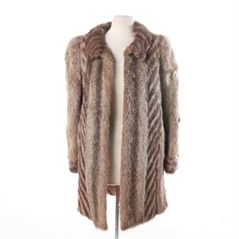 Women's Raccoon Fur Coat by Krakowskie Zaklady Futrzarskie: A women’s raccoon fur coat by Krakowskie Zaklady Futrzarskie. The collared coat alternates panels of brown and white fur with panels of diagonally striped fur, and has hook and eye closures. The coat is lined to the interior and includes a brand label.