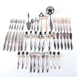 Hefra 'American' Silver Plated Flatware Set: A silver plated flatware set by Hefra S.A. of Warsaw, Poland. This set is in the American pattern, which features an Art Deco-inspired handle with curved arrow motifs. This forty-eight piece set includes five salad forks, six soup spoons, six dinner knives, six teaspoons, six butter spreaders, six cake forks, six dinner forks, a pie server, a sugar spoon, a pick fork, a youth fork, a serving spoon, a place fork, and a ladle. The flatware is marked “Hefra Met-60” to the backs, and the dinner knives are marked “Hefra Stainless” to the blades.