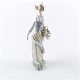 Lladró "Genteel Dutch Girl" Figurine: A Lladró porcelain figurine, titled Genteel Dutch Girl. The figurine depicts a young Dutch woman, wearing a bonnet, dress, and wooden clogs, carrying a basket of tulips. It is stamped “Lladro, Hand Made In Spain” in blue to underside.