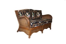 Vintage Wicker Outdoor Loveseat: A vintage wicker outdoor loveseat. The loveseat comes with a cushioned seat and back. The wicker has a medium brown stain to it and the cushion has a tropical motif. The cushion is fully removable. No maker’s marks visible.