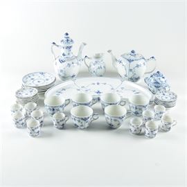 Royal Copenhagen "Blue Fluted" Porcelain Tea Service: A selection of vintage Royal Copenhagen Blue Fluted tableware from 1950-1979. This selection includes an oblong serving tray, a teapot, a coffee pot, a creamer, a lidded sugar bowl, eleven coffees mugs with saucers, and six teacups with five saucers featuring a blue and white flower and line design. Each piece is marked “Royal Copenhagen Denmark” to the base.