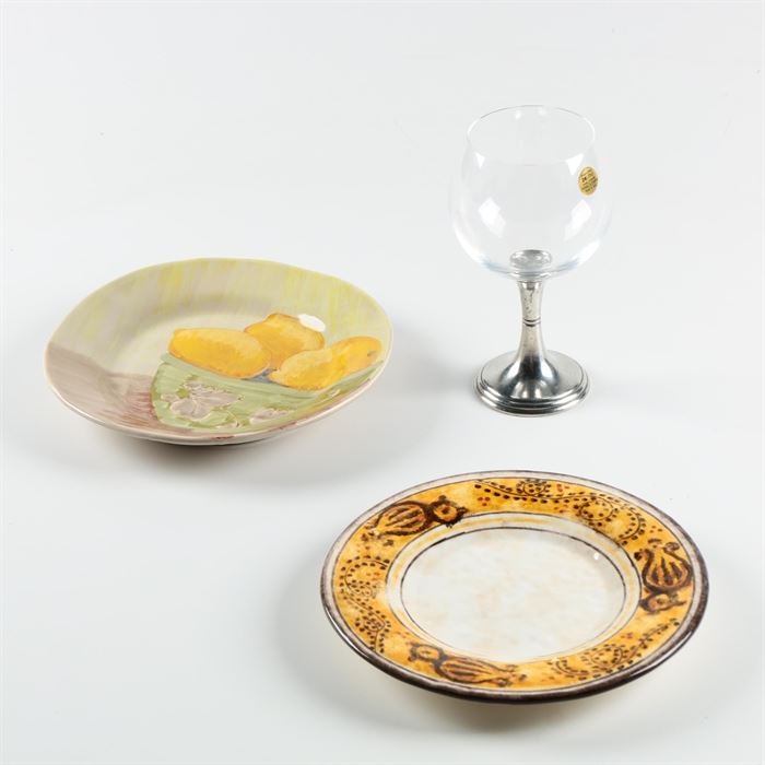 Italian Arte Italica Serveware with Vietri Plate: A group of tableware. This includes an Italian Arte Italica glazed stoneware plate with beige trim. An Italian Arte Italica silver tone and crystal wine glass is included as well as a hand-painted still-life plate with lemons by Vietri.