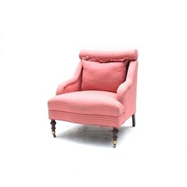 Pink Upholstered Armchair: An upholstered armchair. This pink upholstered chair features a cushioned back over a large seat flanked by arms that rise above trumpet legs with brass casters. The chair is unmarked. This chair matches the chair featured in lot 17IND144-061 of this sale.