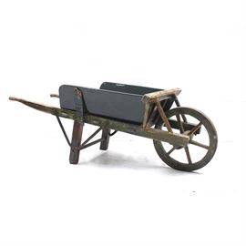 Vintage Wooden Wheelbarrow: A vintage wooden wheelbarrow. The wheelbarrow has a wooden frame and wheels painted in a brown finish. The storage compartment is comprised of wooden slats painted black. The wheelbarrow’s wheel features a wrought iron exterior.