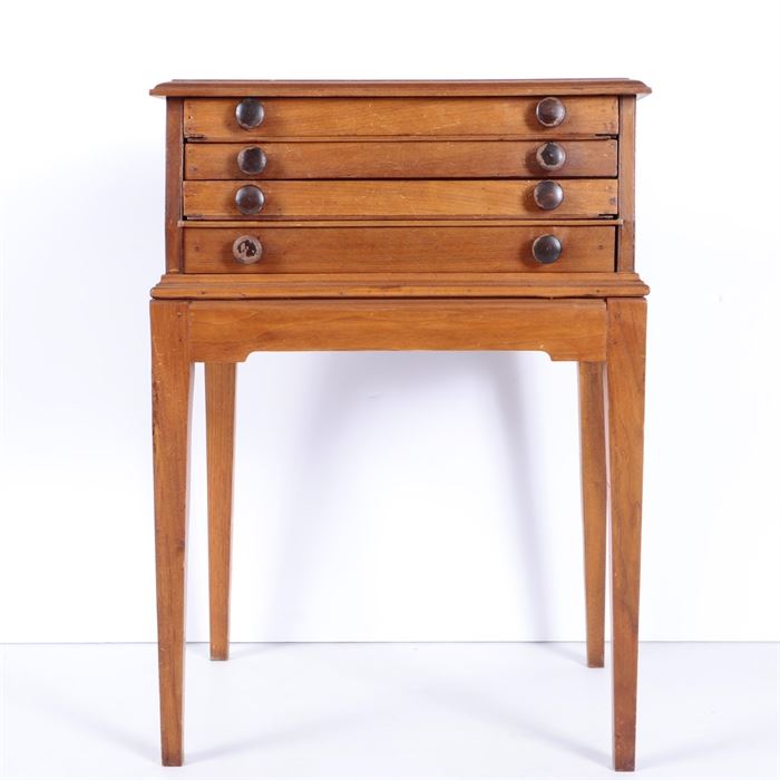 Antique Spool Cabinet: An antique spool cabinet. It has four shallow drawers stacked in a top portion with rounded edges, set on a rectangular table base with plain apron and tapered block legs. Each drawer has two wooden knobs.