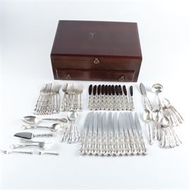 Gorham "Rondo" Sterling Silver Flatware in Chest: A collection of sterling silver flatware by Gorham. This eighty-seven piece set includes twelve hollow handle dinner knives with stainless steel blades, eleven hollow handle butter spreaders with stainless steel blades, twenty-three teaspoons, eleven dinner forks, twelve salad forks, five round soup spoons, two shell sugar spoons, one place spoon, two flat handle master butters, a gravy ladle, a tablespoon, a pierced tablespoon, a hollow handle cake server with a stainless steel blade, a cold meat fork, a flat handle butter spreader, a lemon fork, and an olive fork. These pieces feature the Rondo scroll pattern and each is presented in a mahogany stained wooden flatware chest with brass tone handles. The utensils are marked “Gorham Sterling” and the pattern name and the total approximate weight, excluding the knives with stainless steel blades, is 76.890 ozt.