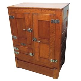Vintage Oak Ice Box by Garland: A vintage oak ice box by Garland. This rectangular top ice box features three cabinet doors of varying sizes with recessed panels, metal hinges, and metal lock handles terminating on a plinth base. The cabinet doors open to a porcelain interior with metal racks in one cabinet. This piece is marked “Garland” to the front.