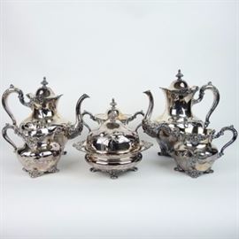 Homan Quadruple Silver Plate Tea Service: A Homan Manufacturing Company quadruple silver plate tea service set, circa 1900. The pattern number is noted as 2245 and features an impressed iris floral design and repoussé trim, depicting a lady with long flowing hair in cameo in the Art Nouveau style. The six-piece set includes a coffeepot, teapot, sugar dish, butter dish, and two creamer vessels. Maker and pattern mark are at the bottom of the vessels. The Homan Manufacturing Company produced silver plate from Cincinnati, Ohio between 1847 and 1941.