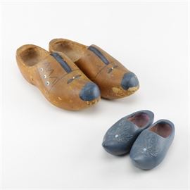 Decorative Wooden Clogs: A collection of two pairs of decorative wooden clogs. The smaller pair feature a blue finish with a floral design to the toe and the larger pair features a lightly stained finish with designs in blue, black and white tones.