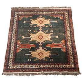 Hand Knotted Kazak Wool Area Rug: A hand woven Kazak wool area rug.. The abrash indigo field is populated with three large linear herati in shades of buff, ochre, sienna, black, and brighter denim blue. From the borders, large motifs in sienna, buff, blue, and black project inward toward the center of the carpet. Two of these are whole and two are halved by the corners of the borders. The complex borders include running-dog, checkered, and sawtooth patterns flanking a primary border with buff background infilled with cruciform motifs and a stylized check-mark type pattern. All are worked in the same palette. Natural wool fringe at each end. Unmarked.