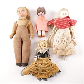 Group of Antique and Vintage Dolls: A group of antique and vintage dolls. The four dolls include: a porcelain doll wearing an off white dress and red striped bib; a composite doll wearing a yellow shirt and brown overalls; a plastic doll depicting a blonde woman with curled hair and makeup in a lace ruffled top and long yellow-brown skirt; and a clay doll with a black veil and pink dress.