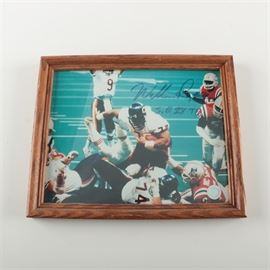 Signed William Perry Chicago Bears Super Bowl XX Photograph: A signed photograph of former NFL Chicago Bears defensive lineman William “The Refrigerator” Perry, taken as he was scoring a touchdown against the New England Patriots during Super Bowl XX. Perry (1962-) was known for his size and athleticism as a player. He was one of the many stars of the 1985 Chicago Bears team, and Coach Mike Ditka, who used him on the offensive squad regularly as a fullback, allowed for the touchdown seen in the photograph. A signature in blue pen is noted at the top right. It is presented under glass in an oak frame, with a sawtooth hanger to the verso.