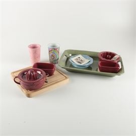 Assorted Longaberger Pottery: A collection of assorted Longaberger pottery. Included in this collection are a paprika colored two piece juicer, two small rectangular paprika colored dishes, and a wooden cutting board with a snowflake in its center. Also included are two travel cups in a pink and multicolored pattern, a small blue plate in the Vintage Vine pattern, a small cake pan in paprika, and a sage green rectangular serving tray with a cutout handle in each end. All items are marked to the bottom.