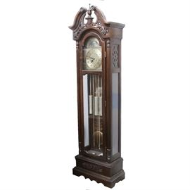 31-Day Wood Grandfather Clock: A thirty-one day grandfather clock. This clock is housed in a mahogany-stained Federal-style wood frame with acanthus openwork and glass panels, which reveal three weights and a harp pendulum. The clock includes a moon-phase-and-constellation dial above the hour face. The hour dial features Roman numerals over a silver-tone, scrollwork embellished metal panel. A key is not included. The clock has not been tested.