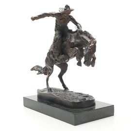 Brass Sculpture After Frederic Remington's "Bronco Buster": A bronze sculpture after the sculpture by Frederic Remington (1861-1909), the very popular American West artist of the 19th century. This striking piece, titled Bronco Buster, depicts a wild horse trying to throw his rider while the hardened cowboy stays in the saddle to break this bucking bronco. The base is engraved with a reproduction signature. Back of horse is branded with a triangle in a circle brand. The sculpture has been mounted onto a marble base.