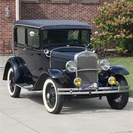1930 Model A Ford Tudor Sedan: A 1930 Model A Ford Tudor sedan, serial number A1396152, with an odometer reading of 16478. This 1930 Model A features an inline four-cylinder engine with non-synchronized three speed transmission. The sedan has a black vinyl top, a two-tone deep blue and black body with a red pin stripe, the original brown mohair upholstery, a set of Firestone 4.75″ × 5″ × 19″ wide white-wall tires, a spare wheel mounted to the rear, two-light headlamps with blue bulbs. Chrome Ford step plates are located on both running boards, and a chrome eagle radiator cap. The six-volt starting system has an optional crank start. The vehicle has three speeds forward with one reverse. This vehicle is suited to drive, show, or parade.