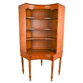 Heywood-Wakefield Corner Cabinet With Matching Chair: A Heywood-Wakefield corner cabinet. This mid-century cabinet features a curved front with a shaped top rail over three fixed shelves with plate grooves, and a single dovetailed drawer to the curved apron. It is raised on five turned legs with bun feet. A matching desk chair with an off-white vinyl seat is included. These items are located on the lower level of the home with walk-out access up an exterior flight of wide stairs; it will require assistance in moving.