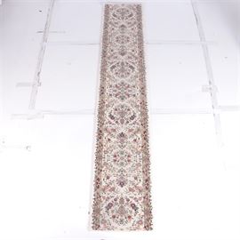 Floral Runner Rug: A floral runner rug. This machine-made item has a central pattern of floral inspired medallions in shades of pink, red and green against a white ground. The rug features a border with a complementary color scheme. A short fringe is present at both ends. The rug does not present a manufacturer’s mark.
