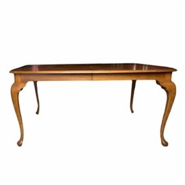 Queen Anne Style Dining Table: A Queen Anne style dining table. The oak table features a rectangular top with curving edges. The table rests on cabriolet style legs and comes with two leaves.