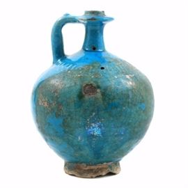 14th-Century Persian Pottery Bottle: A 14th-century Persian pottery vessel with a lustrous turquoise glaze. Around the collar appears a band of calligraphic text. The bottle has a squared handle and footed base.