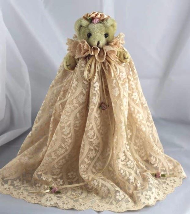 Victoria-249. Victorian Creations. In Synthetic-It  beigh standing at 5.13" H in excellent conditon.  Small bear on a stand in a champagne beige lace  christening dress with ribbons and fabric flowers.  Trimmed peach ribbon hat.
