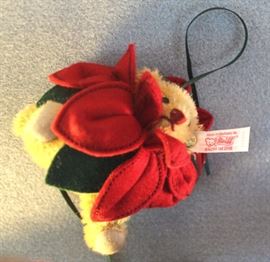 Steiff Poinsettia Bear Ornament 624 in blond  mohair.  He has jtd. arms and legs and a head that  will turn.  His eyes are black and a red  embroidered nose.  Around his neck he wears a red  and green hand stitched felt flower petals collar.
