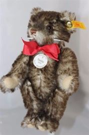 Steiff Teddy Bear - Happy (Anniversary)-Mini-Teddy  1926-73.  Jtd. grey brown tipped mohair plush  miniature bear with light tan flannel paw pads.   It has a white historic chest tag, "Teddy 1926".   With a red ribbon neck bow.

