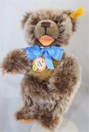 Steiff Teddy Bear - Zotty (1951) Mini-95.  Jtd.  white tipped caramel mohair bear with tan flannel  paw pads and flesh toned open mouth.  Wears a  yellow elephant historic chest tag, "Zotty 1951."   Yellow ear tag and a blue ribbon neck bow.
