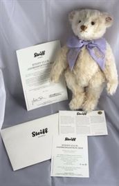 Steiff Creme Edition 2010-293.  The Steiff Club  Annual Edition 2010 collector's bear wears a  lavender ribbon bow around it's neck.  The ribbon  ends are embroidered in gold thread with "Steiff  Club" and "Edition 2010".  
