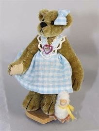 Milly (with duck)-226 Bear with Duck.  Friends  Collection from Little Gem Teddy Bear.  Small bear  wears a baby blue and white check pinafore with  matching headbow.  She stands on a small heart  stand with duck at her feet.
