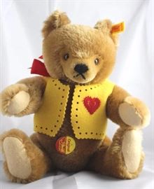 Luv Bear-er (Valentine)-580 Brown Bear.  Wears a  yellow felt vest decorated with a red embroidered  heart.  His neck bow is red silk.  Has a round  yellow/red chest tag. Size:  14" H
