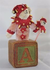 Jess-tee-200.  Tan Jester Bear on Antique Block  with Rose Body.  Wears a wine suede capelet with  gold beads.  A matching cap with bell.  Holds a  teddy staff.  Ltd. #8 of 8. Size:  4 1/2" H
