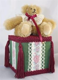 Music Box Bear-201.  Jester Bear with white lace  ruffle threaded with burgundy ribbon bow and  bells.  Sits on green satin and burgundy velvet  music box trimmed with tapestry ribbon and  burgundy tassels.  The bear sways with the music.
