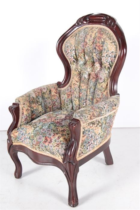Upholstered Wooden Doll's Chair with Floral Pattern: An upholstered wooden chair with a floral pattern. This enclosed armchair features a curved headrest, scrolled arms with padding and cabriole legs. There is a materials tag to the underside of the seat.